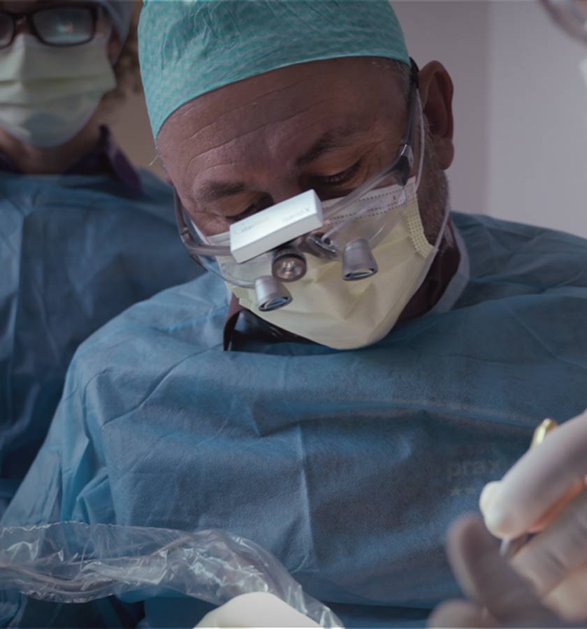 Dr. Gal mit OP-Haube und Lupenbrille während der Implantatbehandlung eines Patienten.