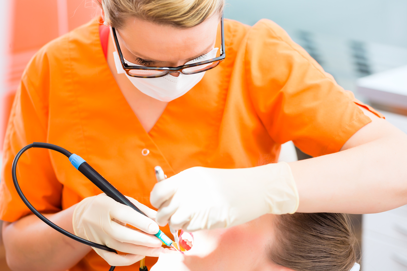 Zahnarzthelferin in oranger OP Kleidung für bei Patientin professionelle Zahnreinigung durch