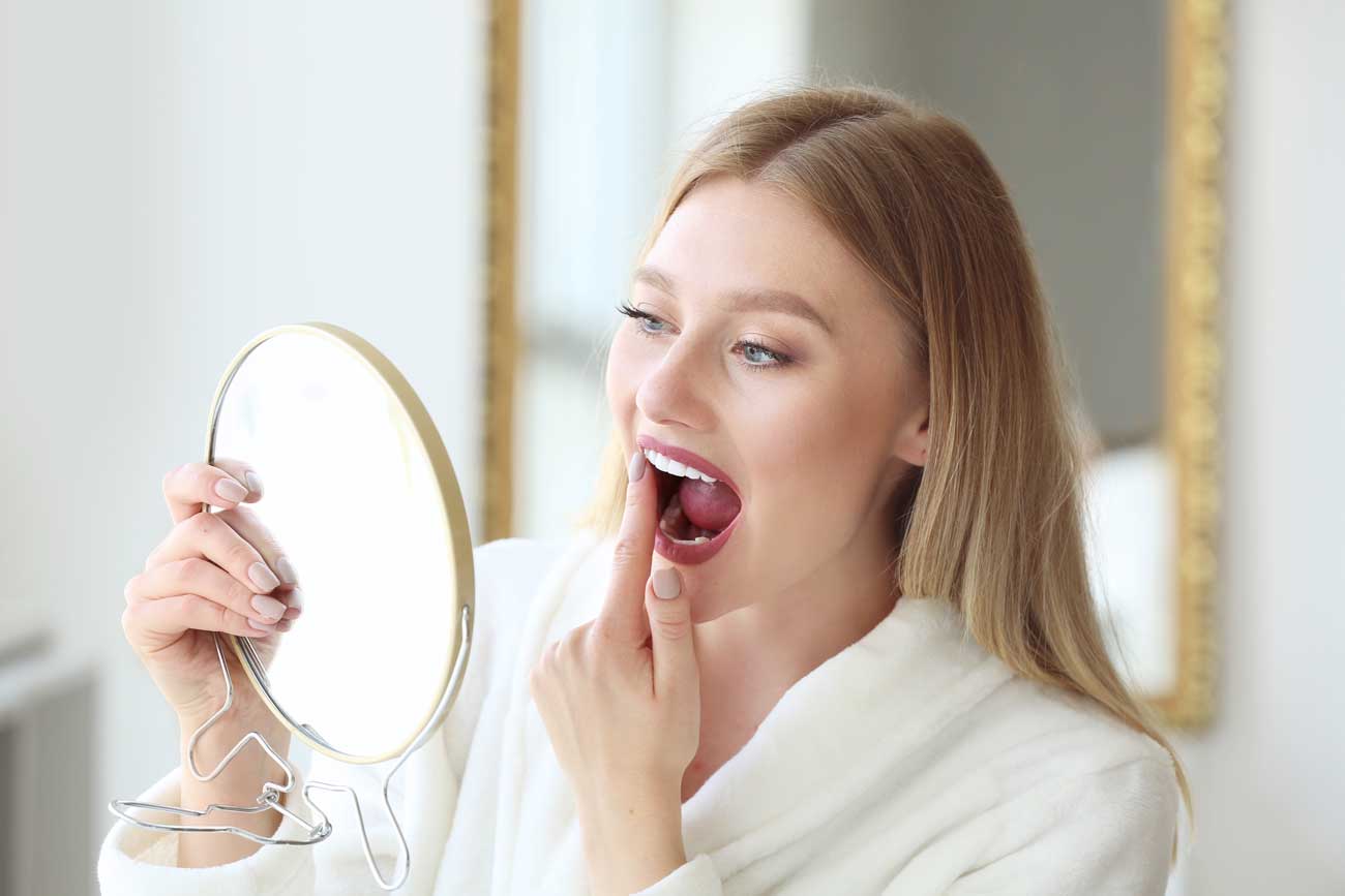 Frau mit einem Kosmetikspiegel prüft ihr Zahnfleisch